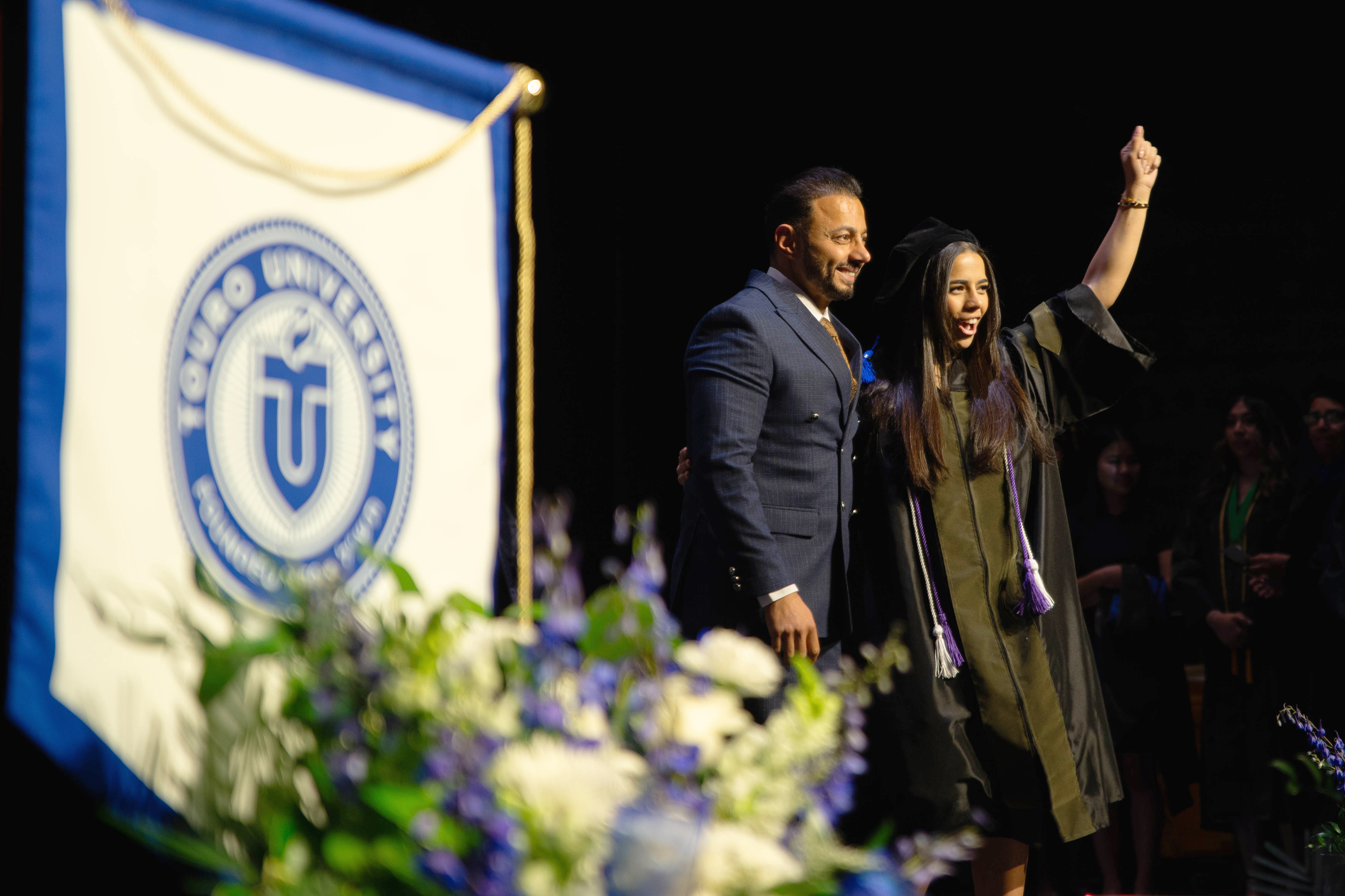 Dr. Sandy Elgendy celebrates with her hooder as she walks across the commencement stage after receiving her Doctor of Pharmacy.