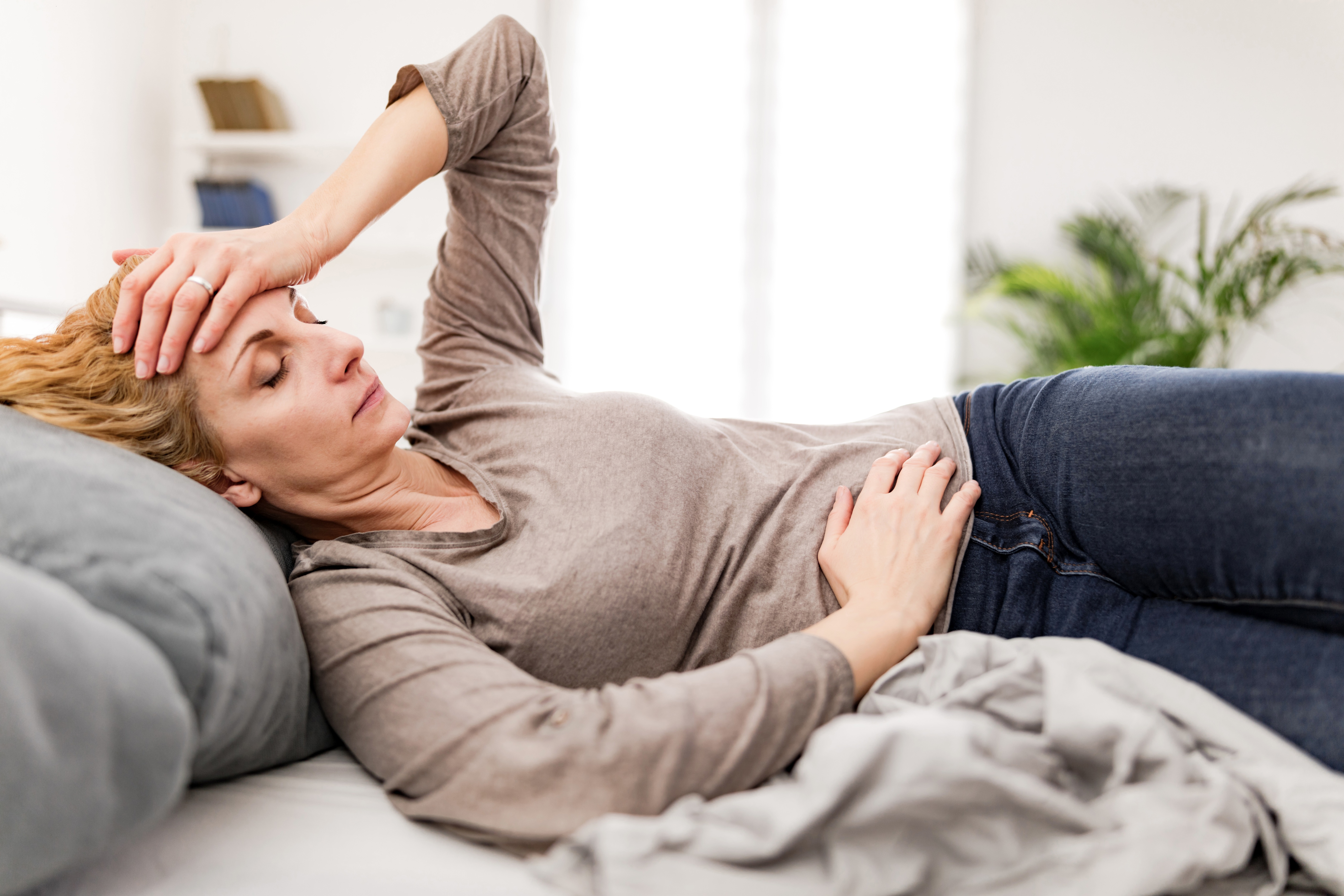 Woman laying down on bed with sickness symptoms