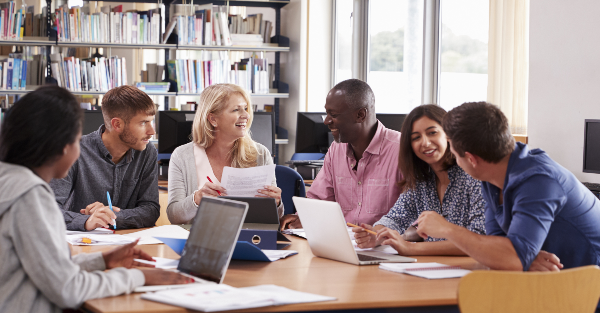 Small group of adults having lively discussion with laptops and papers.