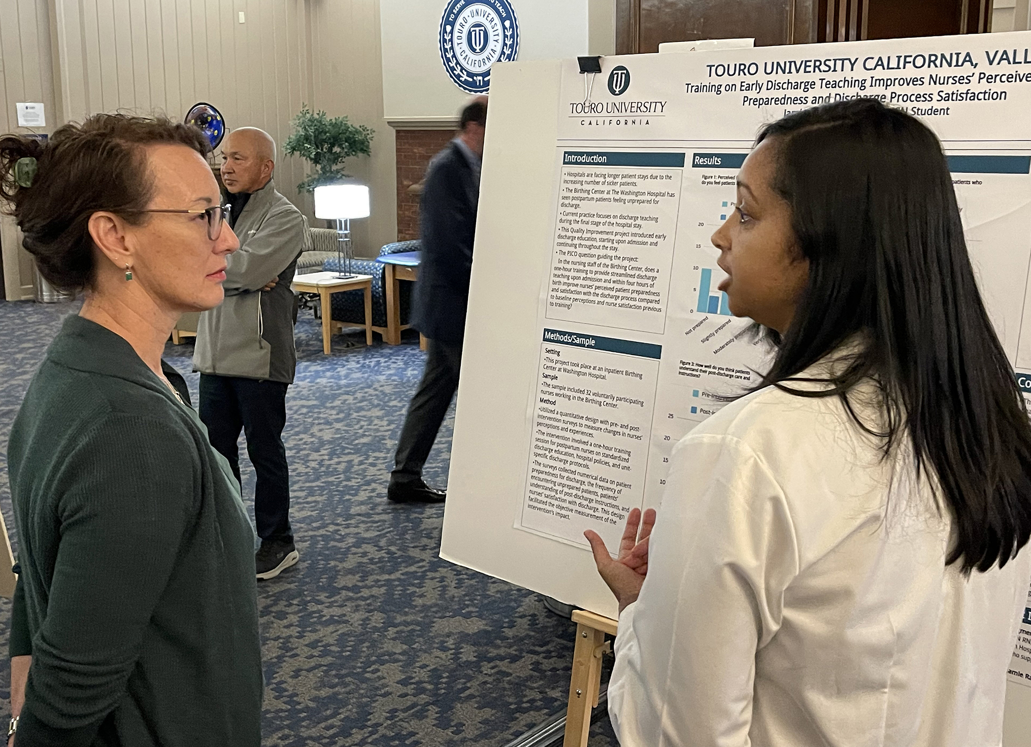 A photo shows School of Nursing Class of 2019 Alumna Jennifer Veler, left, as she listens to new MSN Alumna Jamie Rankin present her poster during the School of Nursing\'s Capstone Poster Presentation and MSN Culmination event in Farragut Inn on campus, Dec. 18, 2024. Rankin is also a member of TUC\'s new Psychiatric Mental Health Nurse Practitioner certificate program.