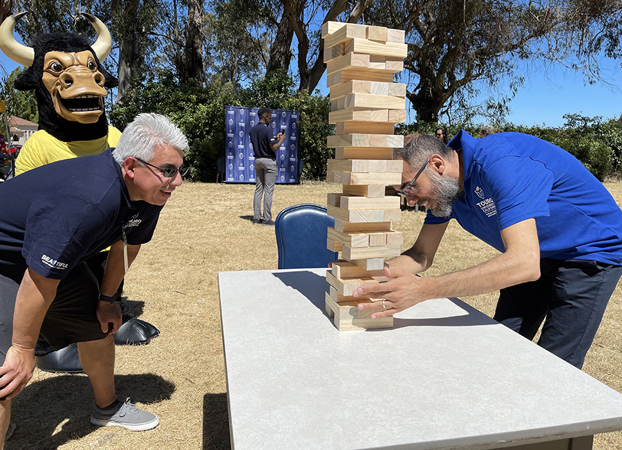 A photo shows Dr. Farid Khalafalla, right, Associate Dean of the College of Education and Health Sciences, as he prepares to pull a piece from a Jenga tower as Pedro Martinez, Associate Dean of Enrollment Management, and the Touro mascot look on during the Spirit Day kickoff in The Grove for Touro University California faculty and staff, Wednesday, Aug. 14, 2024.